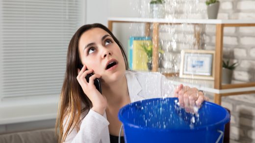 woman calling a Burbank plumber holding a bucket under leaking ceiling